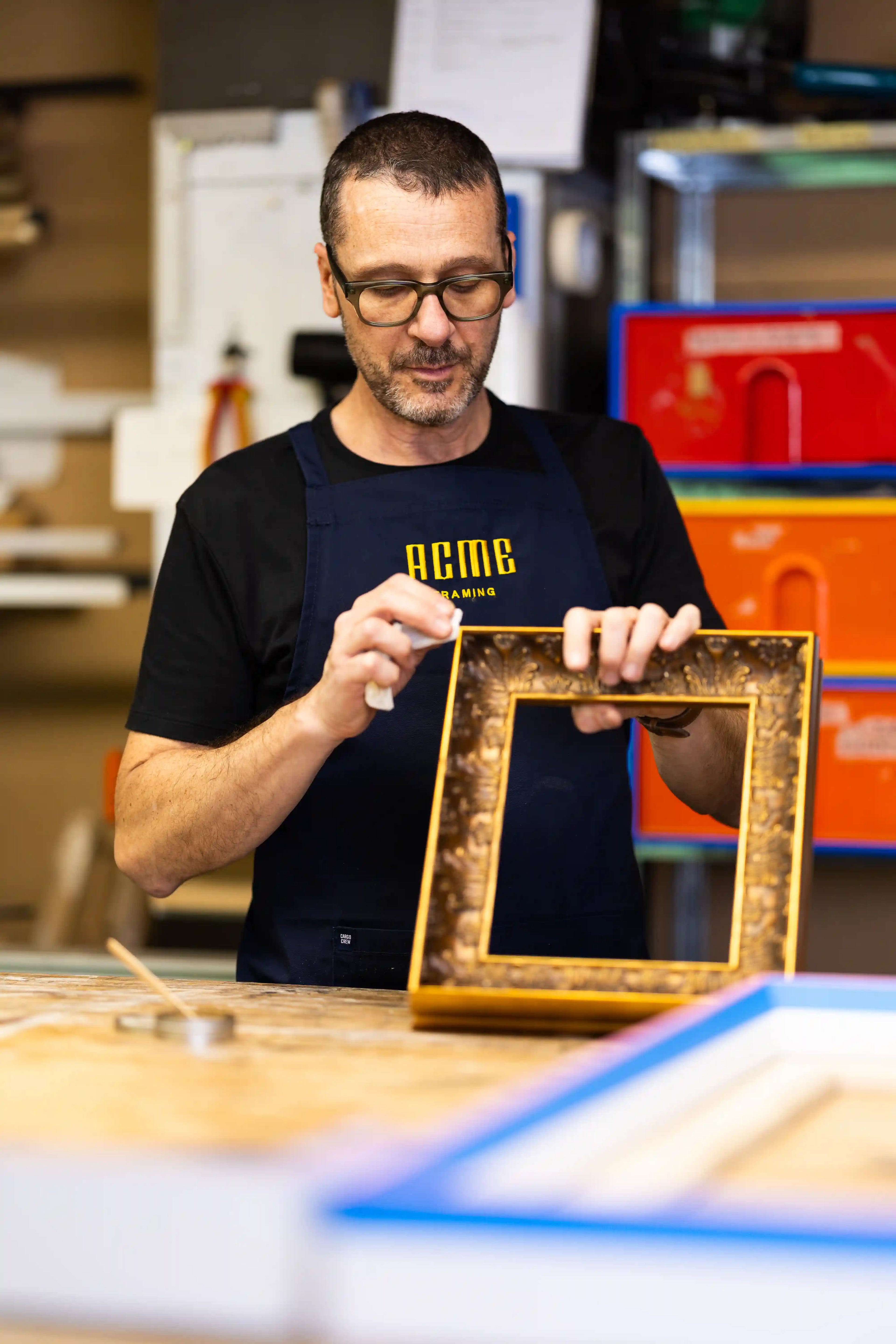 ACME Framing craftsman hand-finishing an ornate bespoke timber picture frame using traditional techniques in a workshop before custom framing an artwork.