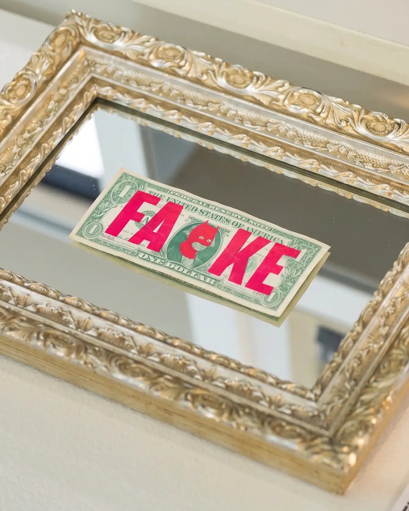 Handcrafted ornate antique silver picture frame displaying a framed one-dollar banknote artwork with bold pink lettering, showcasing intricate carved moulding, metallic finish and bespoke framing craftsmanship.