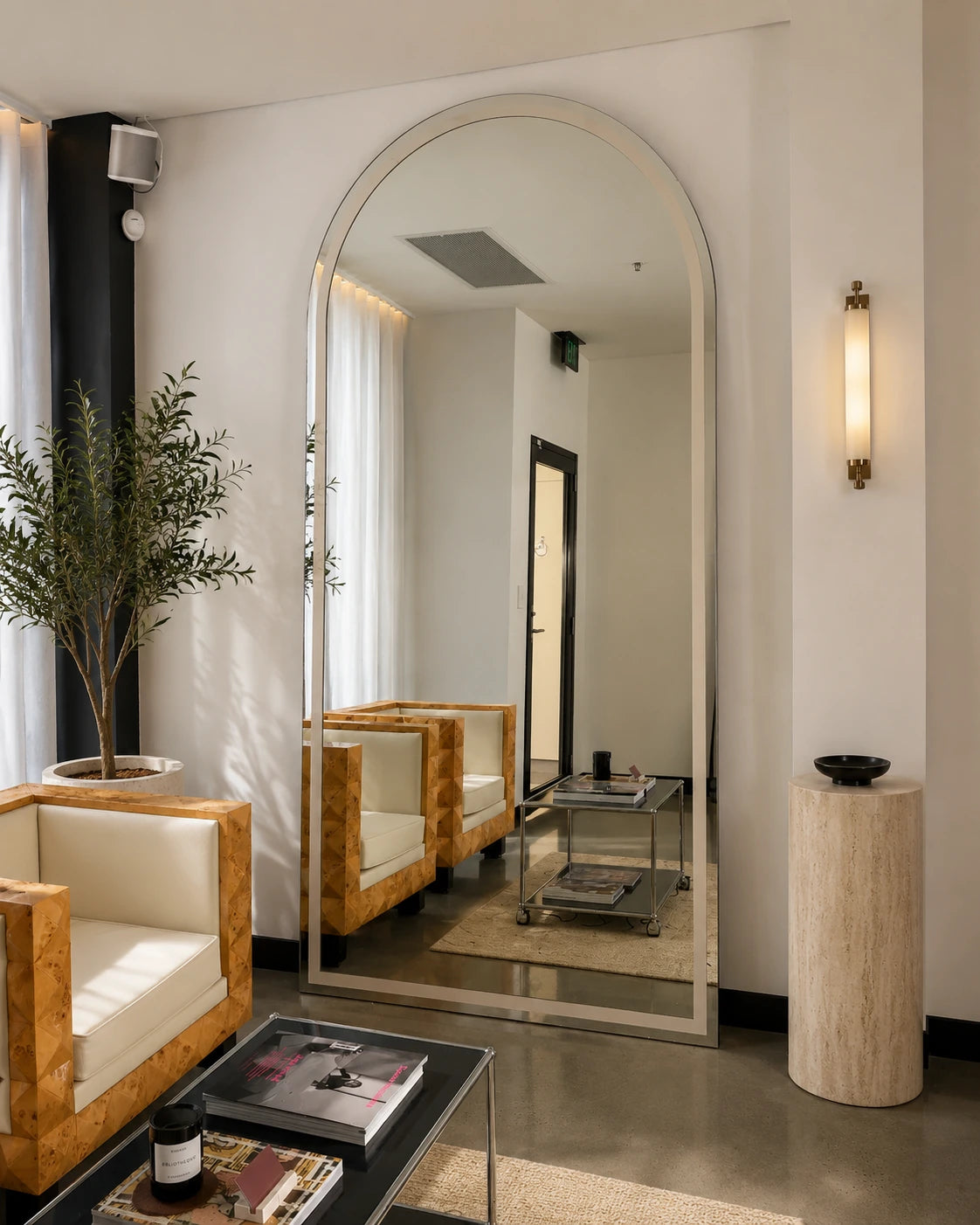 Handcrafted modern arched floor mirror with a slim brushed metal frame, styled in a contemporary interior with timber armchairs, natural stone accents and minimalist décor.